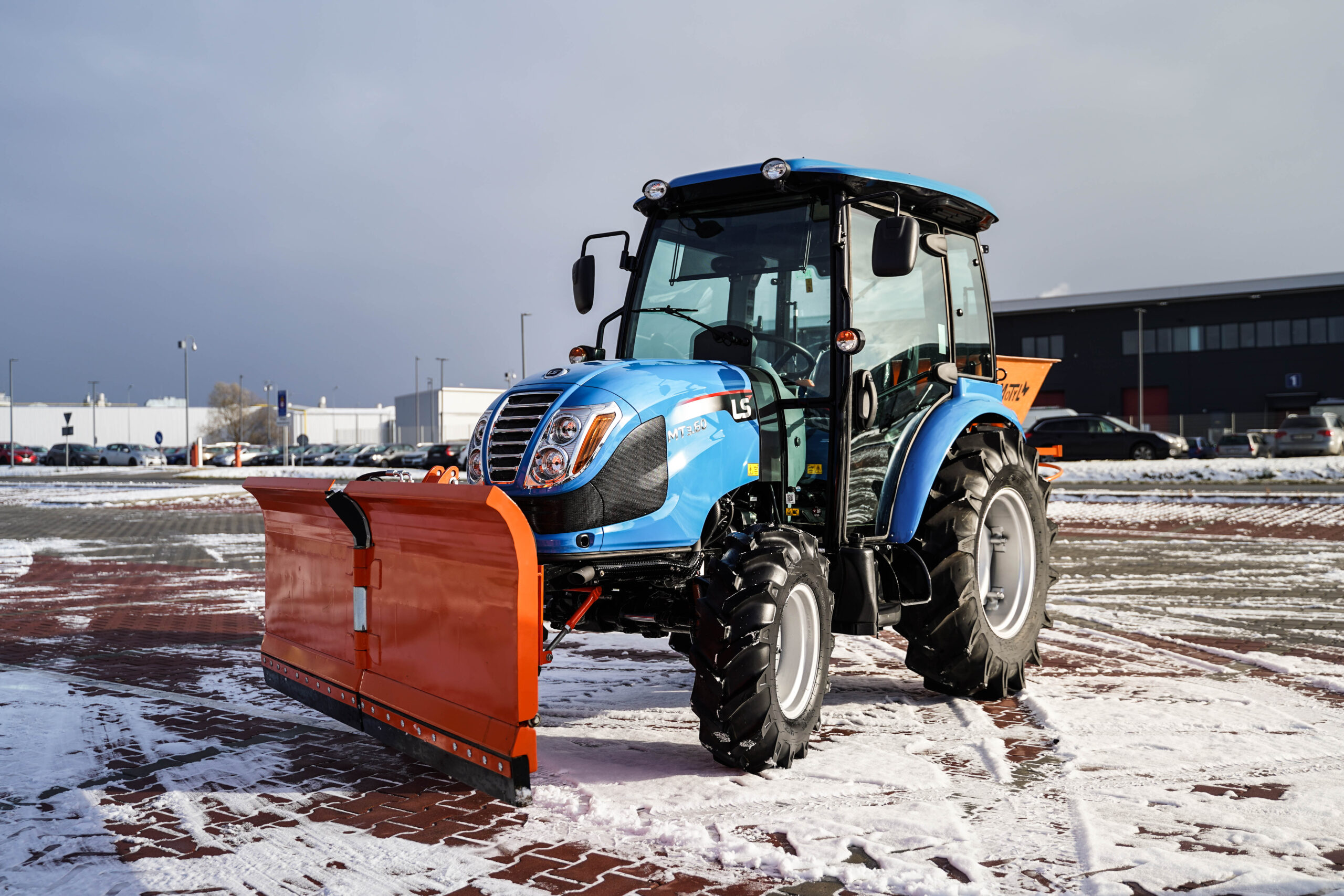 Traktor na odklízení sněhu se šípovým pluhem a sypačem písku