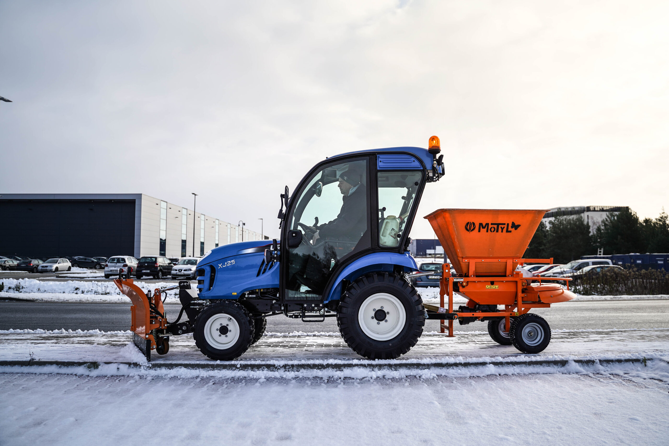 Traktor na odklízení sněhu se šípovým pluhem a sypačem písku