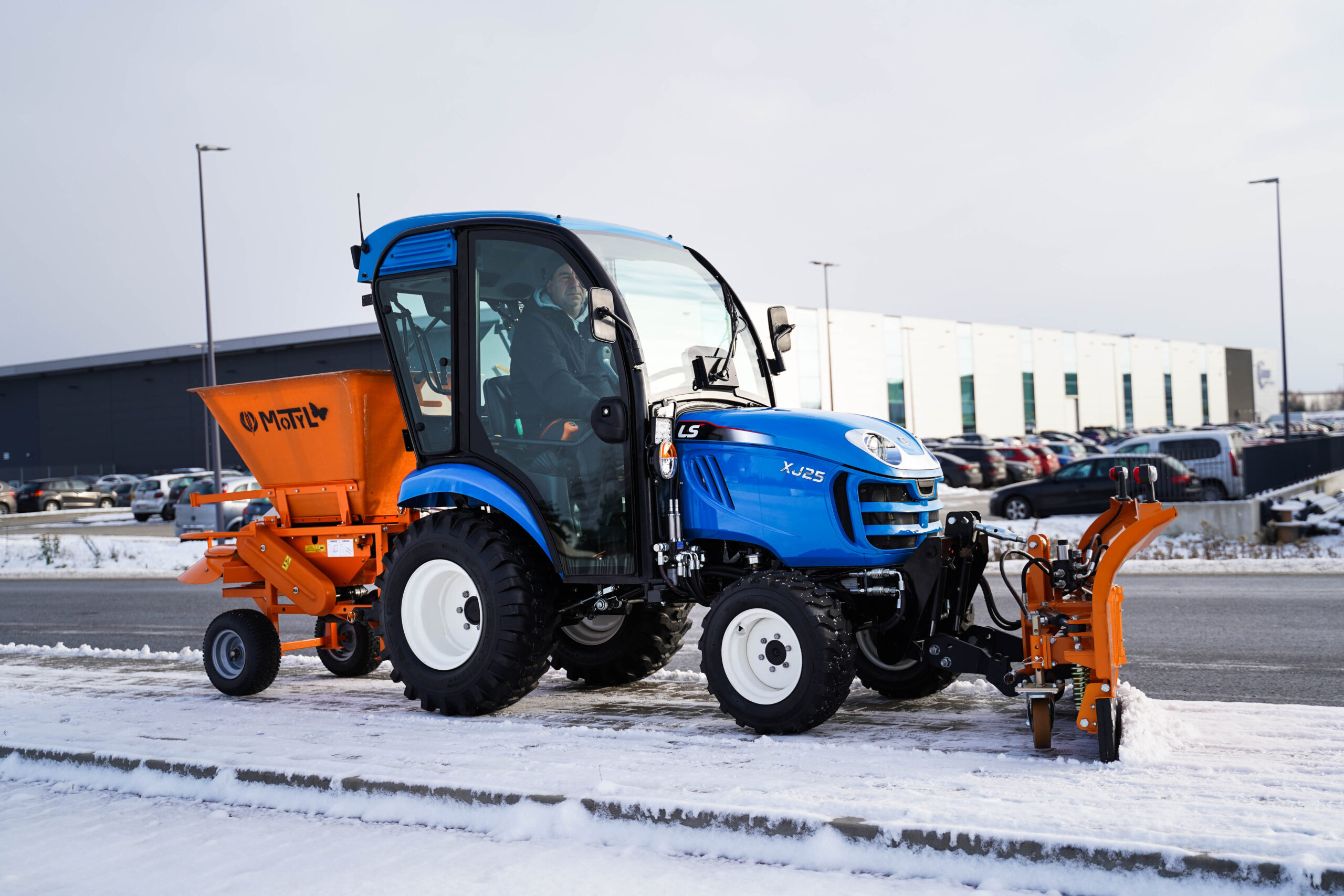 Traktor na odklízení sněhu se šípovým pluhem a sypačem písku