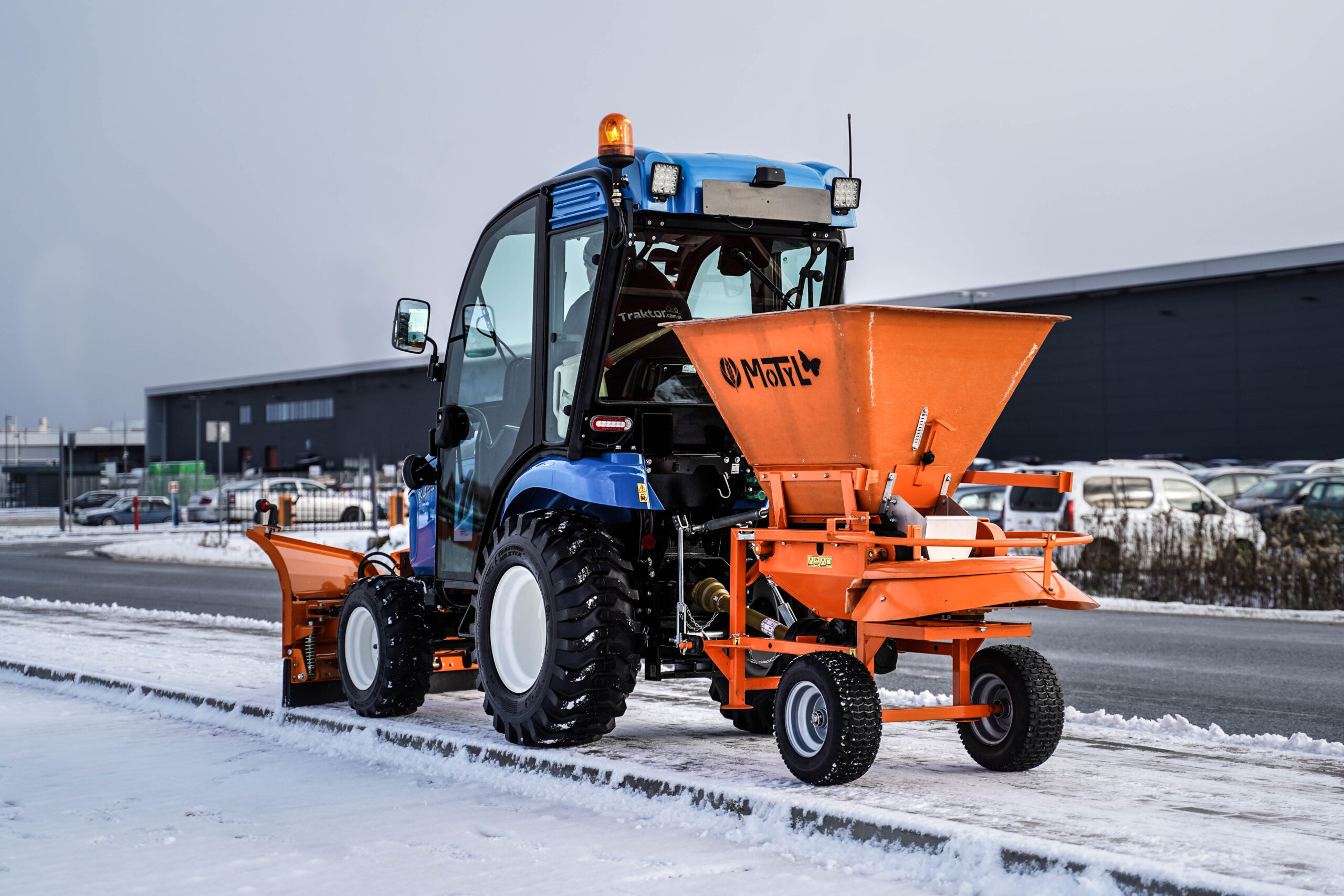 Traktor na odklízení sněhu se šípovým pluhem a sypačem písku